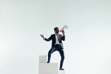 Celebrating corporate victory. Successful businessman shouting with a megaphone while standing at the top of a staircase. Businessman cheering while standing at the top of the corporate ladder. - JLPSF10822
