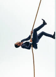 Ambitious businessman climbing a rope that leads to success. Determined business professional working hard to pursue his career goals and aspirations. Businessman climbing up the corporate ladder. - JLPSF10842