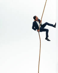 Persistent businessman climbing the rope that leads to success. Business professional working hard to pursue his career goals and aspirations. Ambitious businessman climbing up the corporate ladder. - JLPSF10845