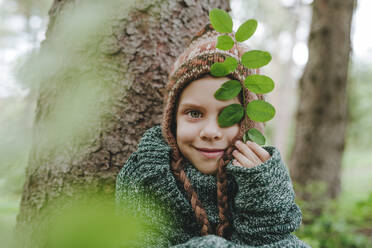 Smiling holding leaves sitting by tree in forest - YTF00226