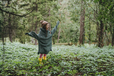 Glückliches Mädchen in übergroßem Pullover inmitten des Waldes stehend - YTF00231