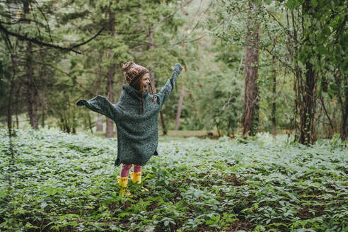 Glückliches Mädchen in übergroßem Pullover inmitten des Waldes stehend - YTF00231