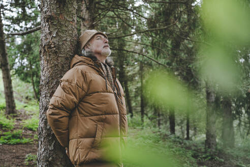 Älterer Mann mit Jacke an einem Baum im Wald stehend - YTF00237