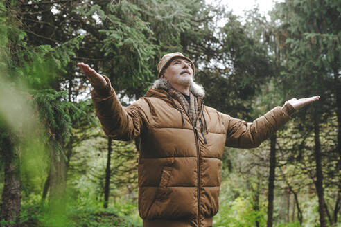 Älterer Mann steht mit ausgestreckten Armen im Wald - YTF00238