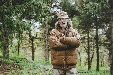 Senior man standing with arms crossed in forest - YTF00239