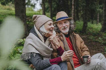 Lächelnde reife Frau mit älterem Mann im Wald sitzend - YTF00265