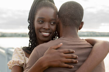 Lächelnde junge Frau, die ihren Freund auf einer Brücke umarmt - JBUF00027