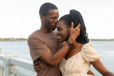 Young man kissing girlfriend by river at sunset - JBUF00029