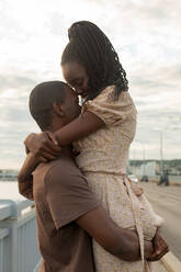 Junger Mann hebt Freundin hoch und umarmt sie an der Brücke - JBUF00033