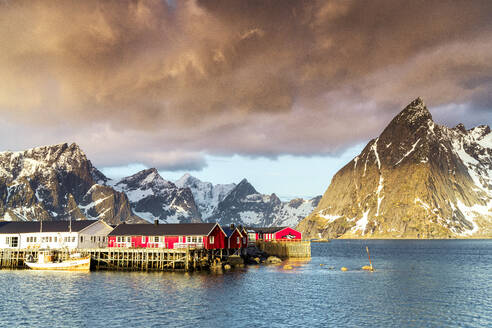 Gewitterwolken in der Morgendämmerung über den Berggipfeln und dem Fischerdorf Sakrisoy, Reine, Landkreis Nordland, Lofoten, Norwegen, Europa - RHPLF23350