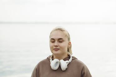 Junge Frau mit geschlossenen Augen meditiert vor dem Meer - JBUF00046