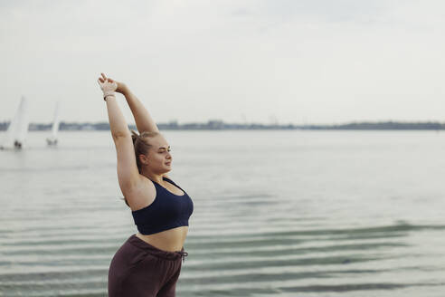 Junge Frau mit erhobenen Händen beim Sport am Meer - JBUF00050