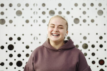 Lächelnde junge Frau mit Bluetooth vor einer Wand - JBUF00057