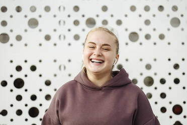 Smiling young woman wearing bluetooth in front of wall - JBUF00057