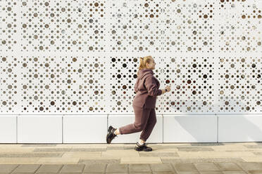 Übergewichtige junge Frau joggt an der Wand - JBUF00060
