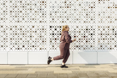 Overweight young woman jogging by wall - JBUF00060