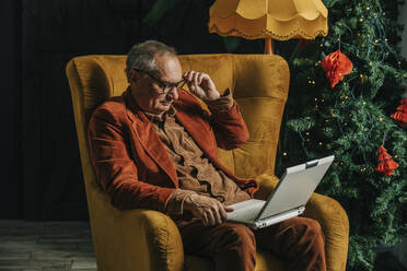 Älterer Mann mit Laptop unter dem Weihnachtsbaum zu Hause - VSNF00034
