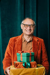 Glücklicher älterer Mann mit Geschenkboxen vor einem Vorhang stehend - VSNF00038
