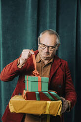 Glücklicher älterer Mann, der vor einem Vorhang Geschenkkartons öffnet - VSNF00039