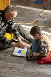 Enkel mit Großvater beim Zeichnen der ukrainischen Flagge auf Papier zu Hause - VSNF00044