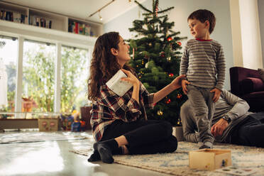 Frau gibt ihrem Sohn ein Geschenk, während sie im Wohnzimmer sitzt. Mutter mit ihrem Sohn feiert Weihnachten zu Hause. - JLPSF10866