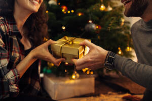 Nahaufnahme eines Mannes und einer Frau, die zu Hause eine Schachtel mit Weihnachtsgeschenken in der Hand halten. Ein Paar tauscht Weihnachtsgeschenke aus. - JLPSF10870