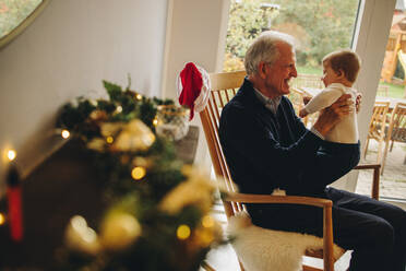 Elderly man with his grandson on a christmas eve. Grandfather holding his grandson sitting on chair. - JLPSF10872