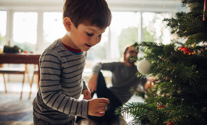 Boy playing by christmas tree. Kids looking for gifts below christmas tree. - JLPSF10902