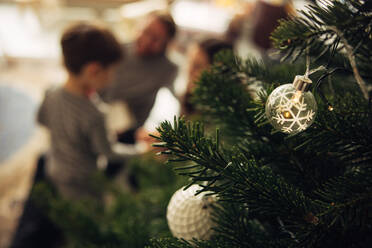 Nahaufnahme eines geschmückten Weihnachtsbaums mit der Familie im Hintergrund. Mit Kugeln geschmückter Weihnachtsbaum im Wohnzimmer. - JLPSF10906