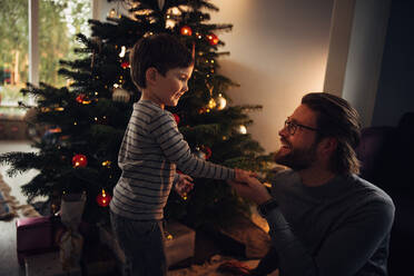 Father and son by a Christmas tree indoors. Family at home celebrating Christmas. - JLPSF10910