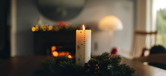 Angezündete Adventskerze mit Kranz auf dem Tisch. Skandinavisches Haus für die Weihnachtsferien dekoriert. - JLPSF10920