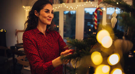 Woman placing decorative items on Christmas tree. Woman decorating Christmas tree inside of a cozy family home. - JLPSF10942