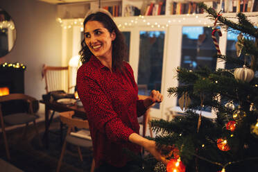 Frau schaut weg, während sie den Weihnachtsbaum schmückt. Frau hängt Schmuck an den Weihnachtsbaum. - JLPSF10944