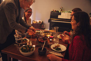 Ein älterer Mann serviert der Familie am Tisch einen gefüllten gebratenen Truthahn. Weihnachtsessen in einem skandinavischen Haus. - JLPSF10961