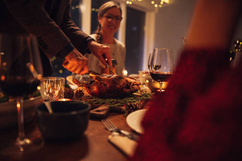 Ein älterer Mann serviert der Familie am Tisch den traditionellen gefüllten gebratenen Truthahn. Familie beim Weihnachtsessen zu Hause. - JLPSF10964