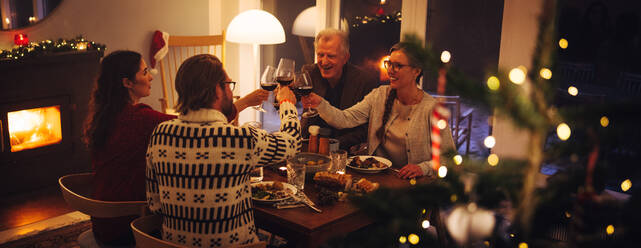 Eine europäische Familie sitzt am Weihnachtsabend am Tisch und stößt mit Wein an. Eine Familie isst zu Hause zu Thanksgiving. - JLPSF10967