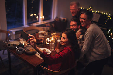 Europäische Familie, die während des Weihnachtsessens zu Hause ein Selfie mit dem Handy macht. Der Fokus liegt auf dem Handy und der weiblichen Hand, die Selfies macht. - JLPSF10970