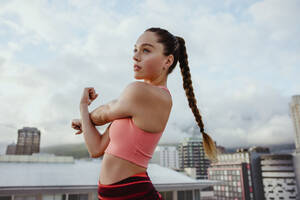Young woman exercising outdoors on rooftop. Sportswoman stretching her arm outdoors. - JLPSF10978