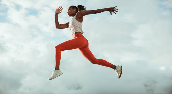 Frau in Fitnesskleidung beim Laufen und Springen Training auf dem Dach gegen den Himmel. Athletische Frau läuft und springt im Freien. - JLPSF10993