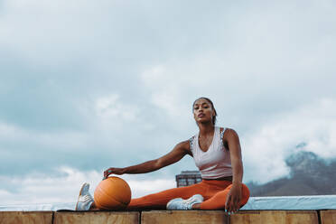 Frau in Fitnesskleidung mit Gymnastikball beim Training im Freien. Sportliche Frau macht Pause vom Training auf dem Dach mit Basketball. - JLPSF10999