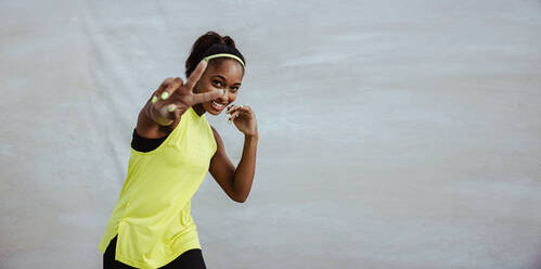 Happy woman in sportswear gesturing peace sign. Female athlete taking a break from workout showing victory hand sign. - JLPSF11015