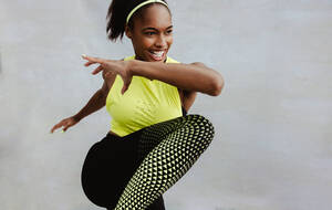Weibliche Athletin in Sportkleidung beim Fitnesstraining. Afrikanische Frau macht Dehnungsübungen und lächelt. - JLPSF11037