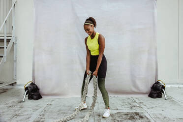 Fit afrikanische Frau in Sportkleidung übt mit Kampf Seil auf dem Dach. Fitness weiblichen tun Kampf Seil Training auf Gebäude Terrasse. - JLPSF11044