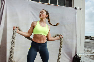 Fit Frau macht Cross-Training Workout mit Battle Rope. Sportlerin trainiert mit Battle Rope auf dem Dach. - JLPSF11047