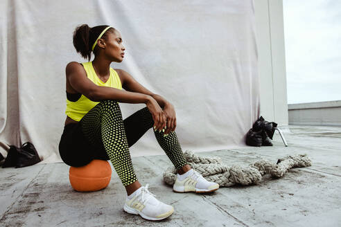 Afrikanische Sportlerin entspannt sich nach dem Training auf einer Gebäudeterrasse. Junge fitte Frau in Sportkleidung, die nach dem Training auf dem Dach eine Pause macht. - JLPSF11062