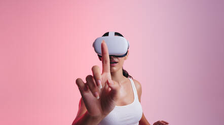 Berührung des Metaversums: Junge Frau berührt mit ihrem Finger den virtuellen Raum, während sie ein Virtual-Reality-Headset trägt. Frau erkundet 3D-Technologie in einem Studio. - JLPSF11076