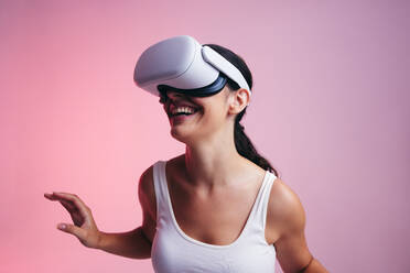 Happy young woman entering a fun virtual reality game in a studio. Woman laughing cheerfully while wearing a virtual reality headset. Female gamer exploring 3D technology. - JLPSF11080