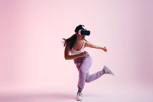 Frau, die das Metaversum erkundet. Aktive junge Frau, die mit Virtual-Reality-Brille und -Controllern spielt. Energetische junge Frau, die eine 3D-Erfahrung in einem Studio macht. - JLPSF11097