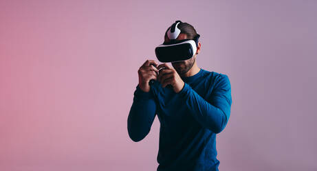 Junger Mann, der ein Virtual-Reality-Boxspiel mit Gaming-Controllern spielt. Aktiver junger Gamer, der ein Virtual-Reality-Headset trägt. Sportlicher junger Mann, der 3D-Videospiele in einem Studio erkundet. - JLPSF11105