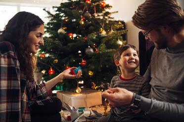 Fröhliche kleine Familie, die zusammen Weihnachten feiert: Vater, Mutter und Sohn sitzen am Weihnachtsbaum und haben Spaß. - JLPSF11118
